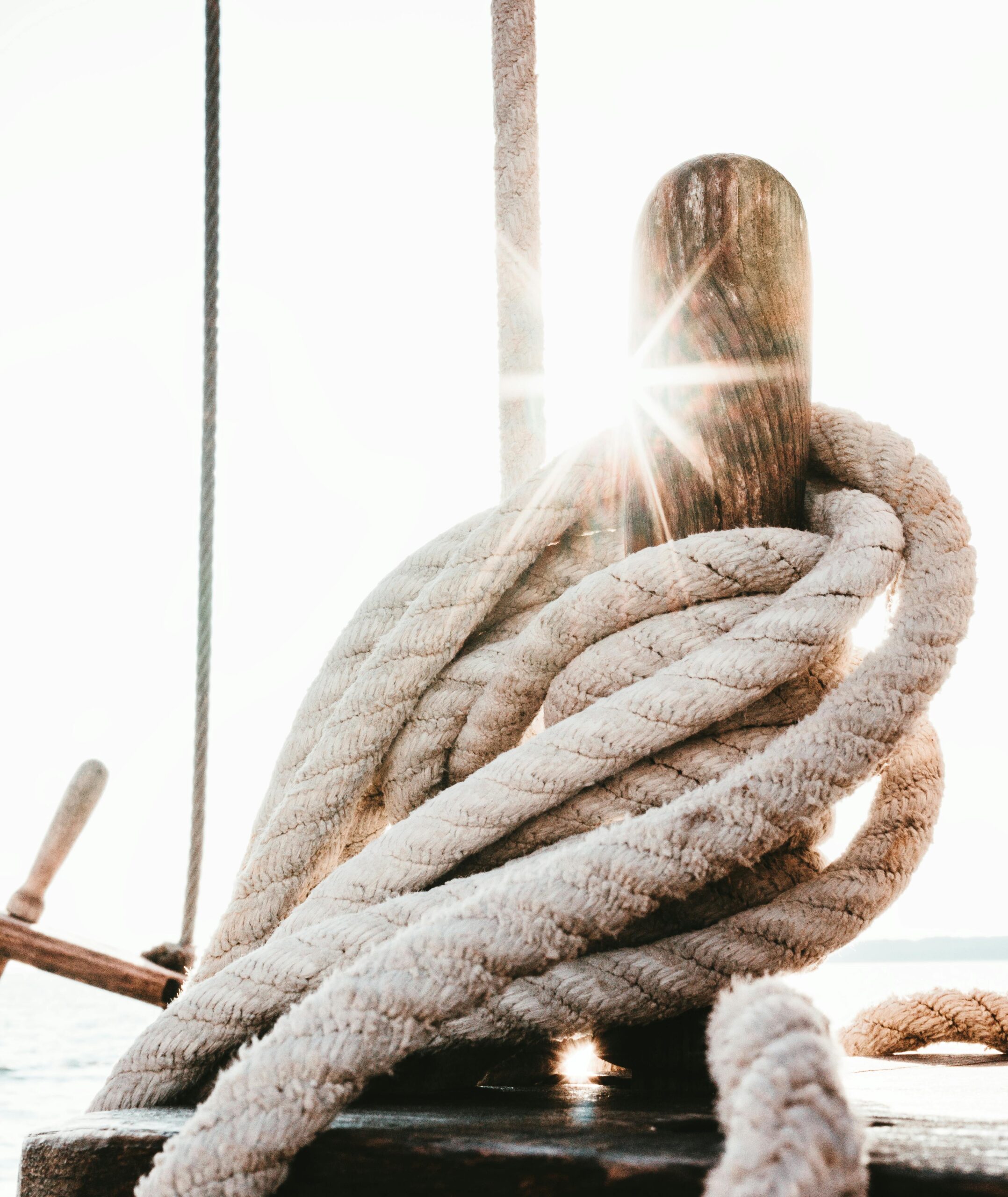 Close-up of sunlit rope coiled around a wooden mast on a boat, capturing nautical adventure.